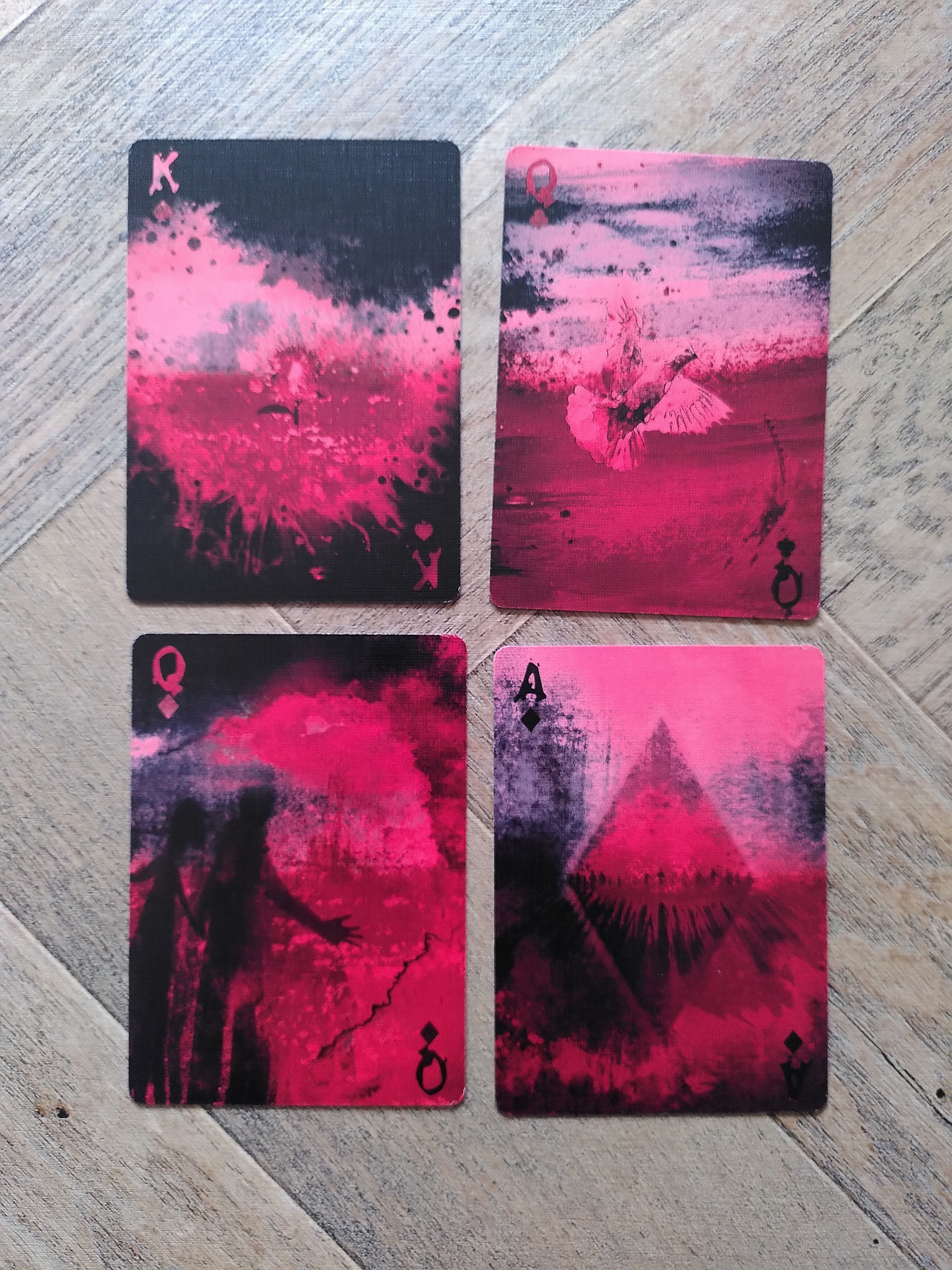 Photo of four playing cards in a deep red and black painted design, each showing various vague images such as shadowy figures and trees.