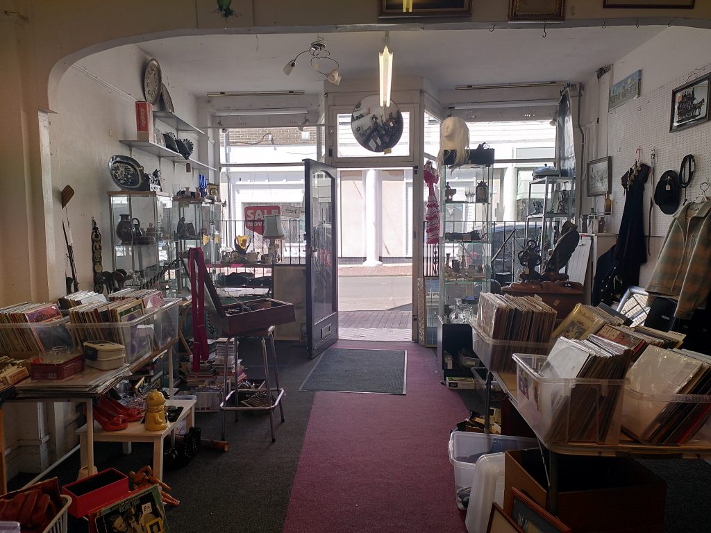The remains of a shop in its closing days, with scattered paraphernalia around and a door leading out into the light of the street beyond.