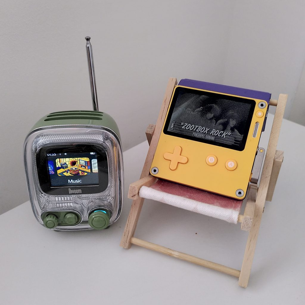 Photo of a Divoom Tivoo retro-TV-styled speaker, besides a yellow Playdate console sitting on a mini deckchair.