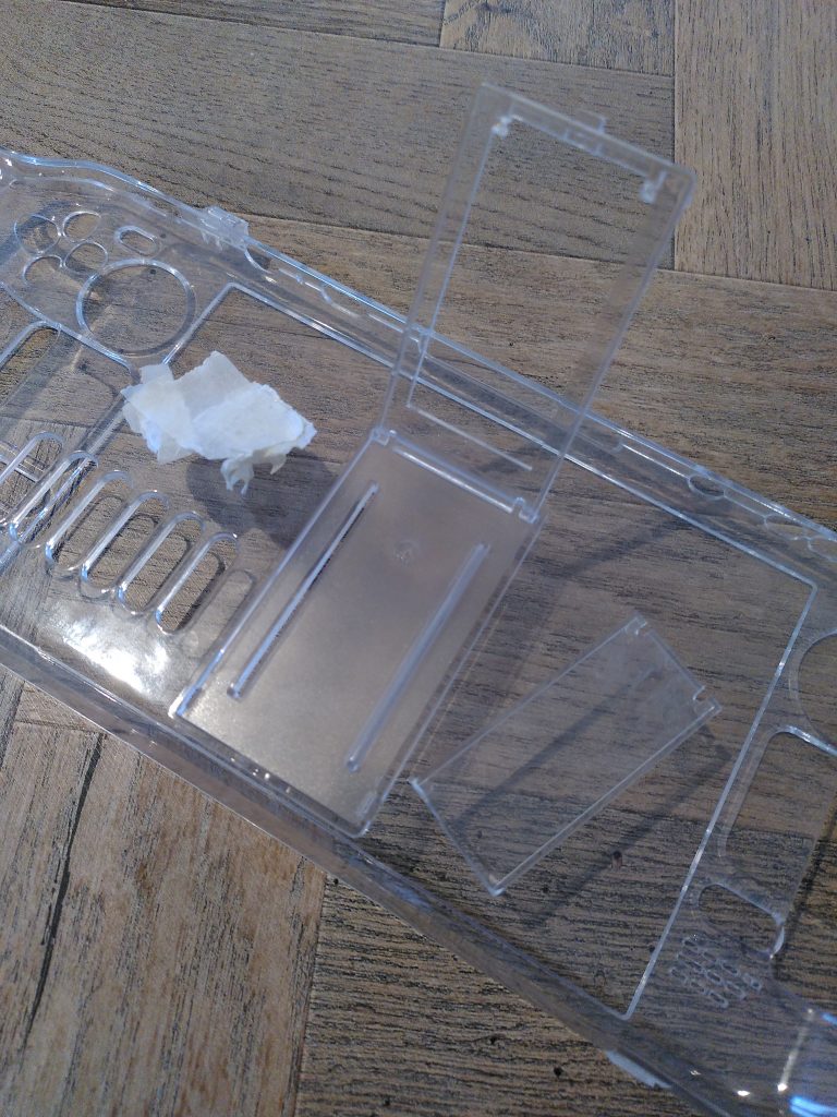 Photo of a clear Steam Deck case with the rear kickstand raised, the broken part to one side and the discarded tape on the other.