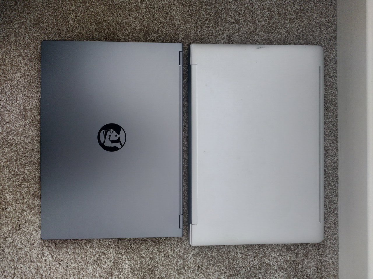 Photo of two laptops next to each other, both closed. One has the logo of Juno computers, a stylised lady's head, in the middle, and is slightly smaller than the other laptop.