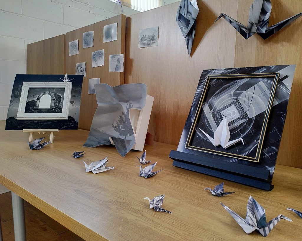 Photo of my 'art' work, a selection of black and white images in different frames and folds, sitting on an array of wood-effect desks.